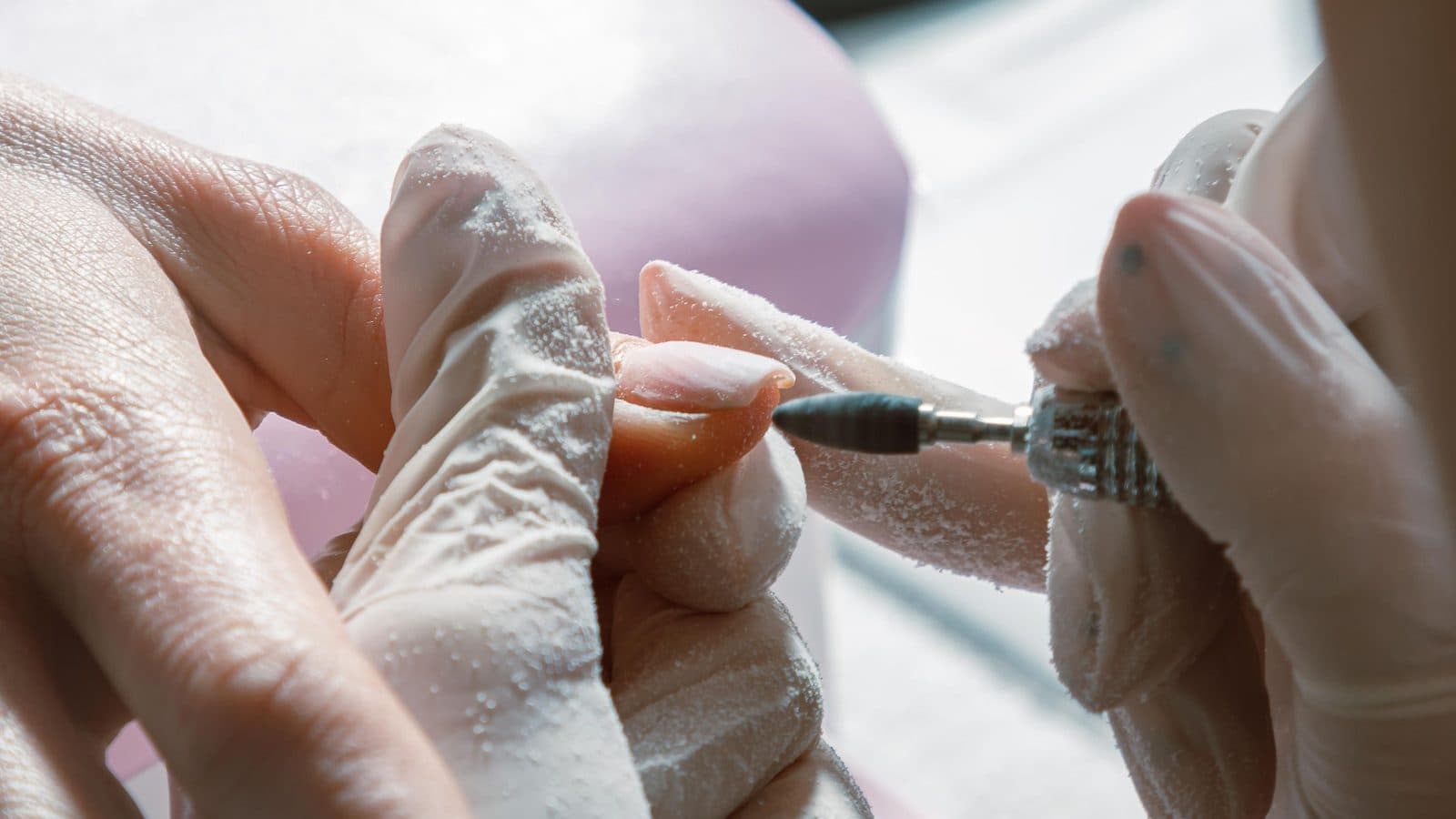 Close-up of a nail technician refining a client's nail plate with an e-file during prep