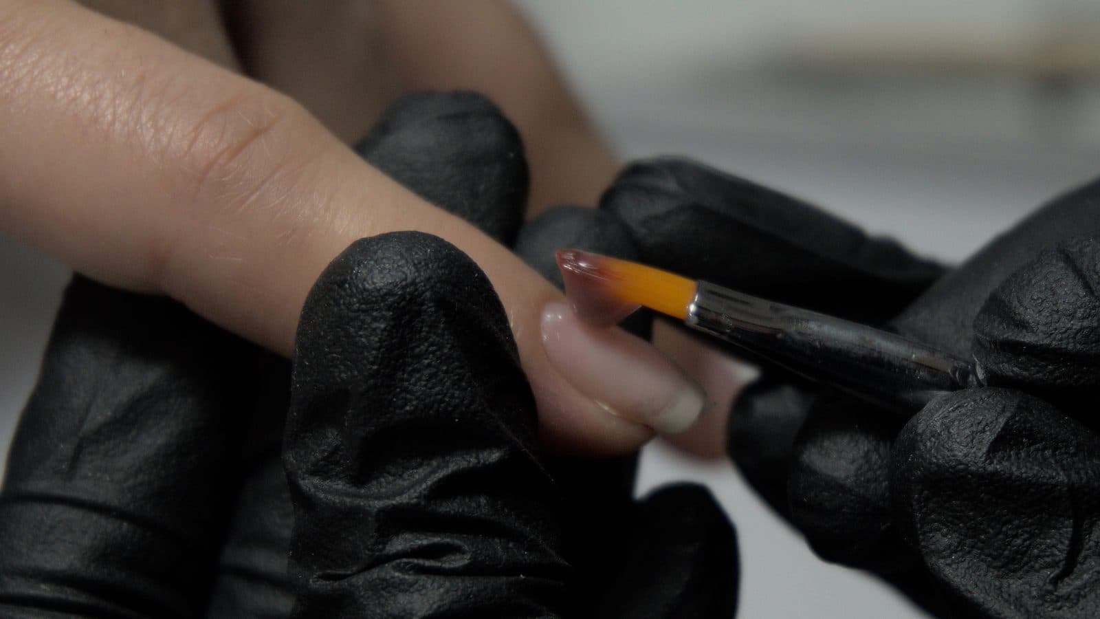 Applying a thin layer of clear builder gel to a single nail with a flat brush