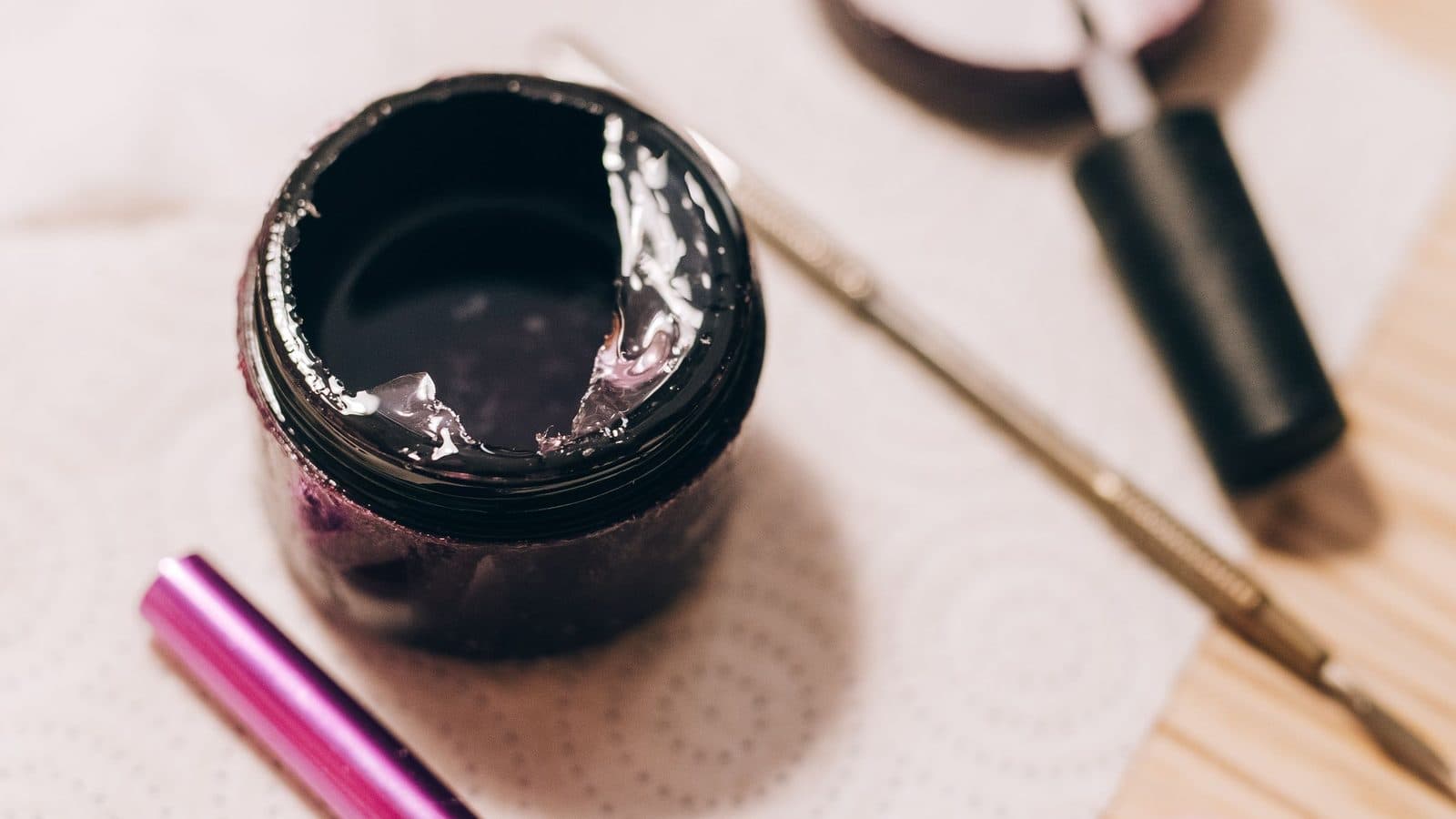 Open jar of clear builder gel with a detail brush and tools on a manicure work surface