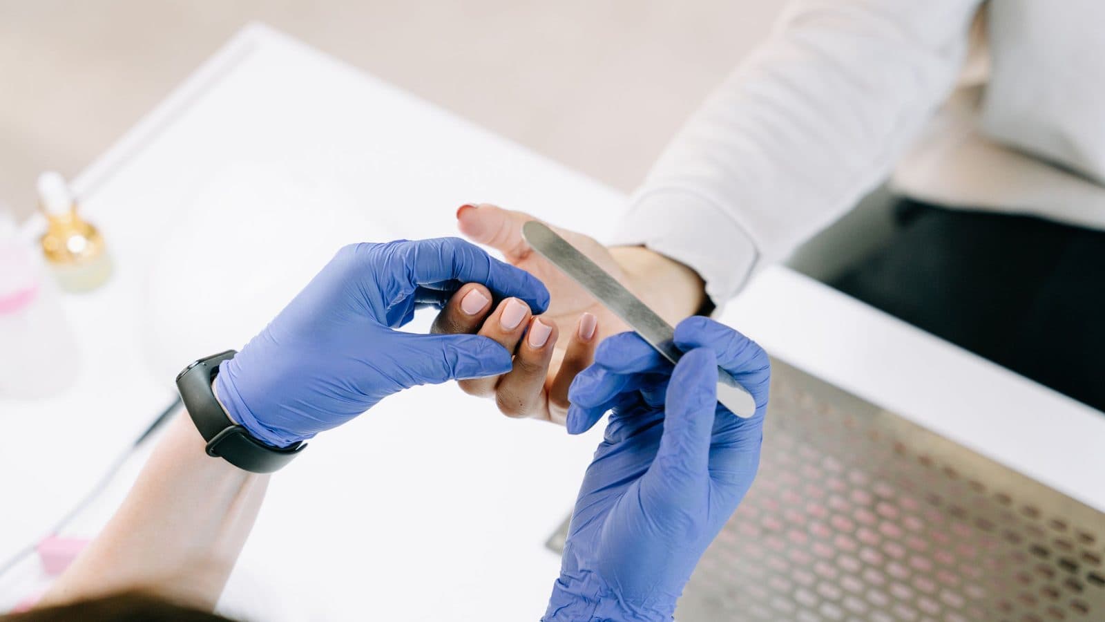 Nail technician wearing nitrile gloves while filing a client's nails at a manicure desk